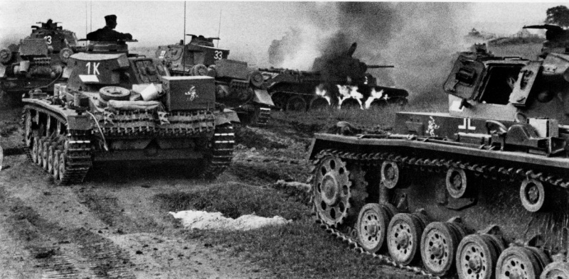 Немецкие танки Pz.III и Pz.IV проезжают мимо горящего советского танка БТ-7. Фото: waralbum.ru